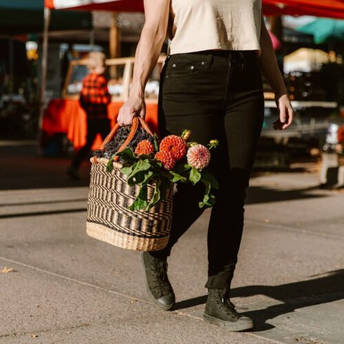 Woman holding dark and natural woven basket with fresh flowers