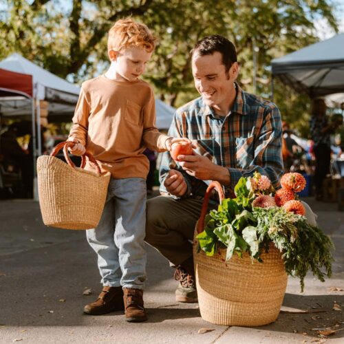 Father and Son picking an apple in a market with shopping totes